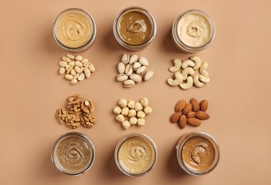 Photo of Many tasty nut butters in jars and nuts on beige table, flat lay