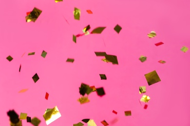 Photo of Shiny golden confetti falling down on pink background