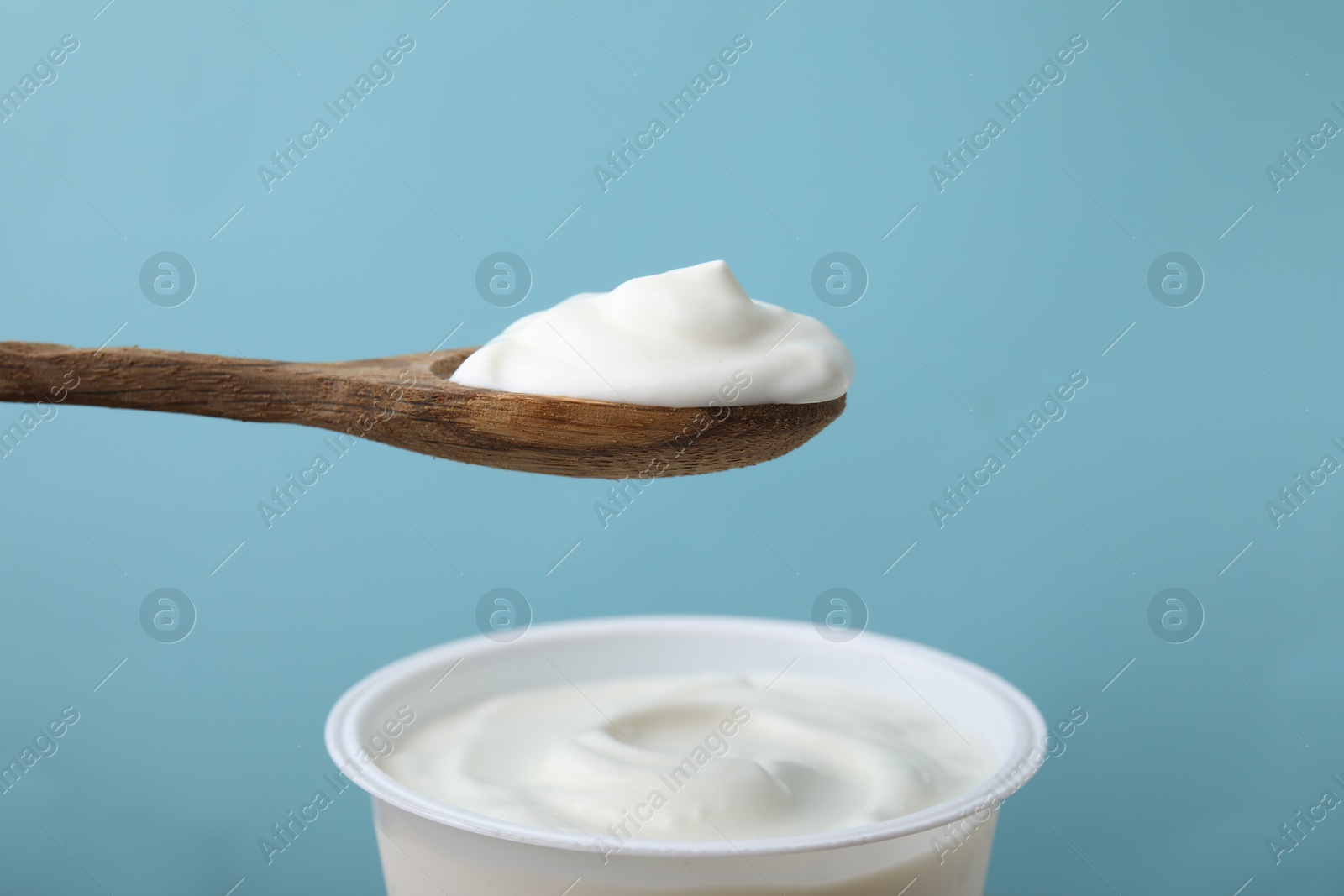 Photo of Eating delicious natural yogurt on light blue background