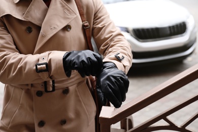 Photo of Stylish man putting on black leather gloves outdoors, closeup