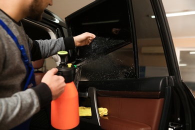 Photo of Worker tinting car window in shop, closeup