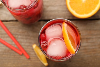 Tasty cranberry cocktail with ice cubes and orange in glasses on wooden table, flat lay