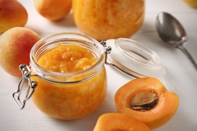 Photo of Jar of apricot jam and fresh fruits on white wooden table, closeup