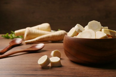 Photo of Fresh ripe parsnip in bowl on wooden table. Space for text