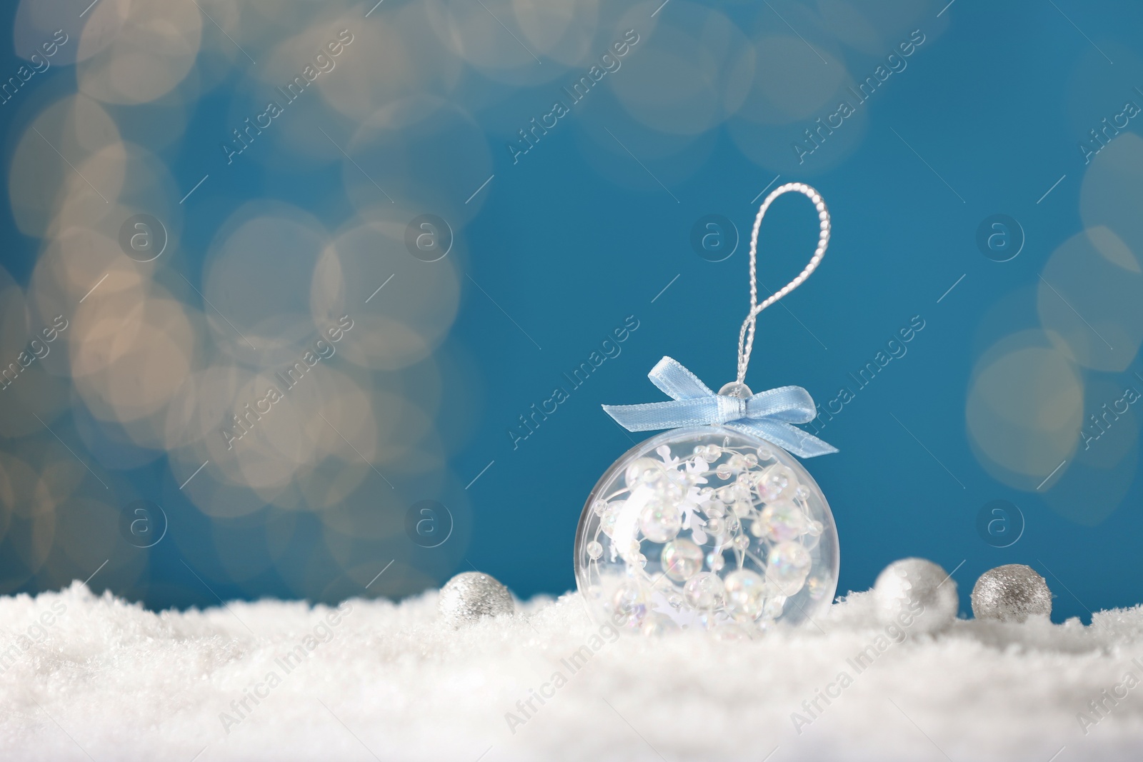 Photo of Decorative snow globe with bright ribbon against blurred festive lights, space for text