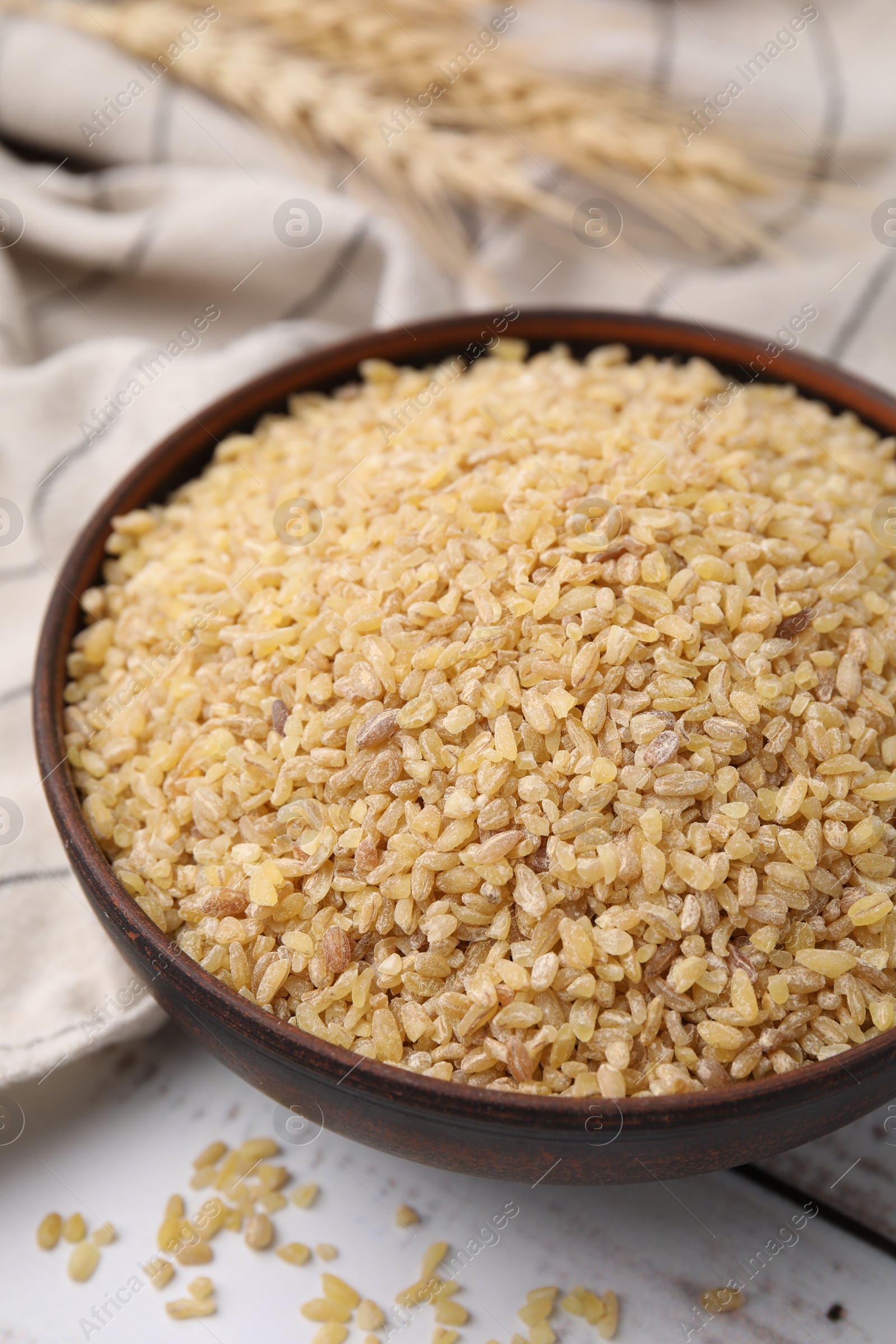 Photo of Raw bulgur in bowl on white wooden table, closeup