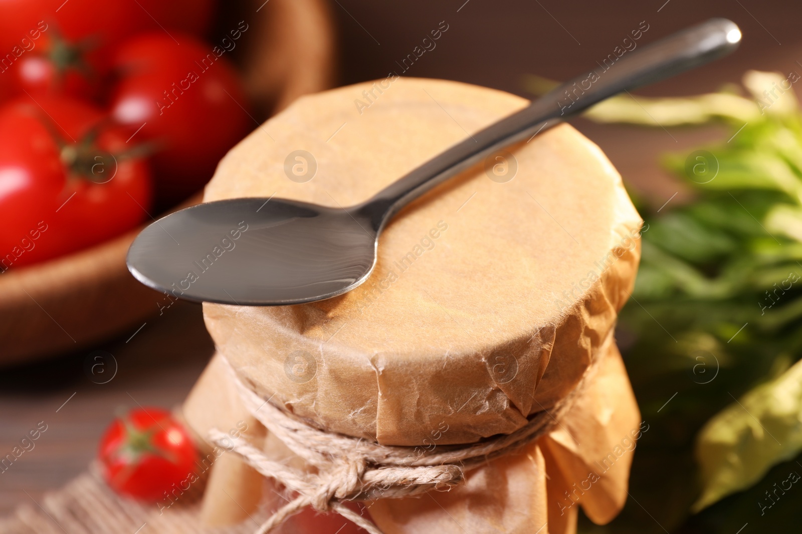 Photo of Jar of tasty tomato paste with spoon on table, closeup