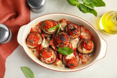 Photo of Baked eggplant with tomatoes, cheese and basil in dishware on light table, flat lay