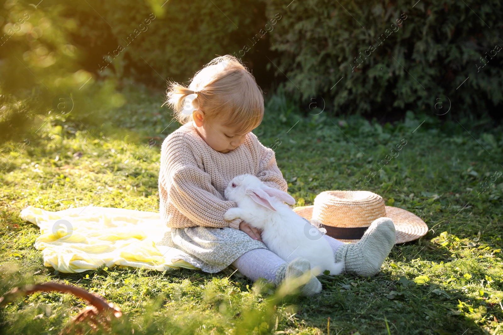 Photo of Cute little girl with adorable rabbit on green grass outdoors