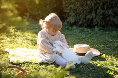 Photo of Cute little girl with adorable rabbit on green grass outdoors