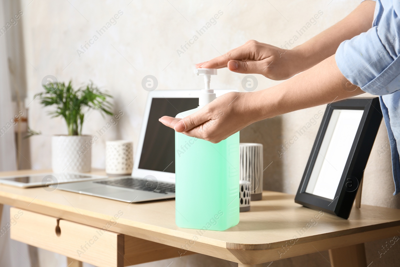 Photo of Woman applying antiseptic gel on hand at workplace, closeup