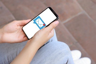Image of Woman received message on mobile phone outdoors, closeup. Envelope illustration on device screen