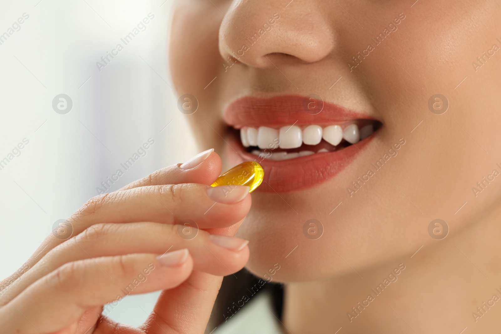 Photo of Young woman taking dietary supplement pill on blurred background, closeup