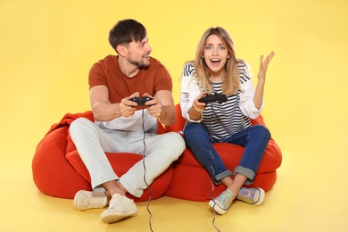 Emotional couple playing video games with controllers on color background