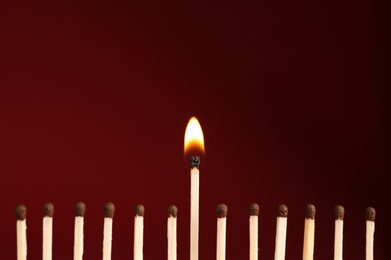 Photo of Burning match among unlit ones on red background, closeup