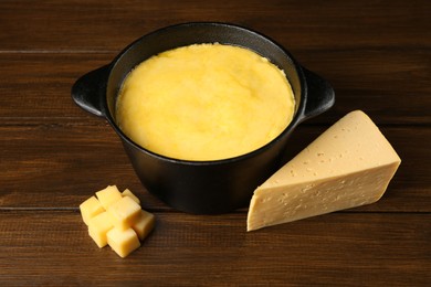 Fondue pot with melted cheese and pieces at wooden table