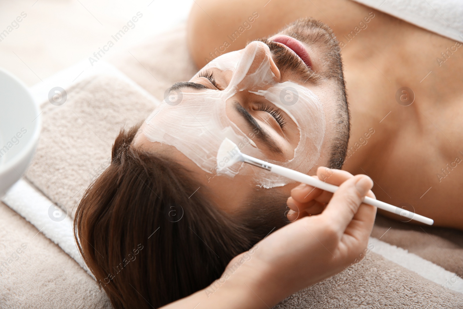 Photo of Cosmetologist applying mask on client's face in spa salon