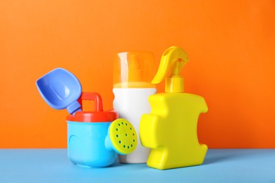 Different suntan products and plastic beach toys on color background