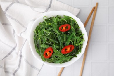 Photo of Tasty seaweed salad served in bowl on white tiled table, top view