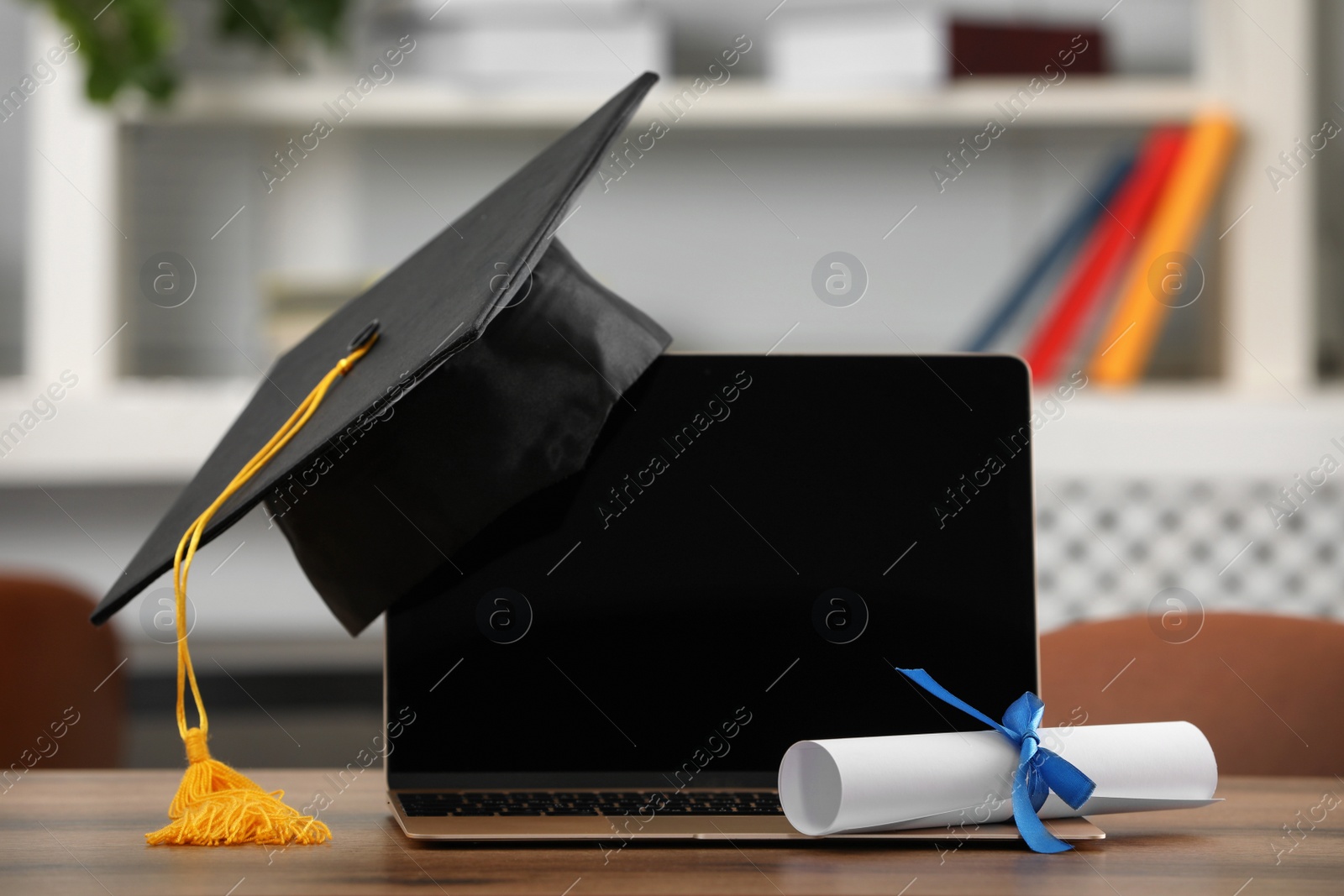 Photo of Graduation hat, student's diploma and laptop on wooden table indoors