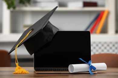 Photo of Graduation hat, student's diploma and laptop on wooden table indoors