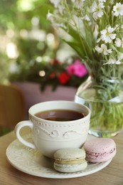 Photo of Cup of  drink, macarons and flowers on table outdoors in morning