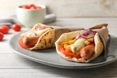 Delicious pita wrap with sausages, vegetables and potato fries on white wooden table, closeup