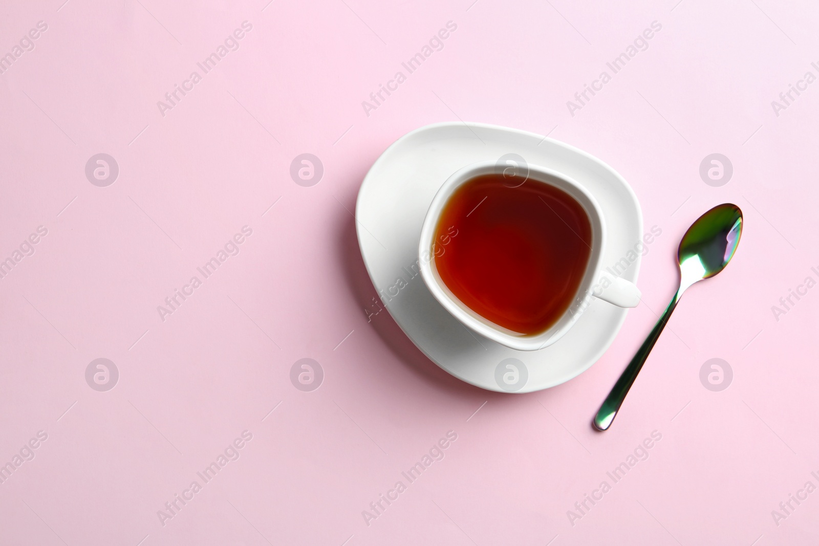 Photo of Cup of tea with saucer and spoon on pink background, flat lay. Space for text