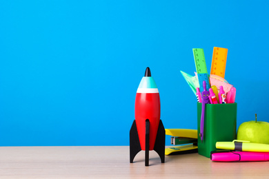 Photo of Bright toy rocket and school supplies on wooden desk. Space for text