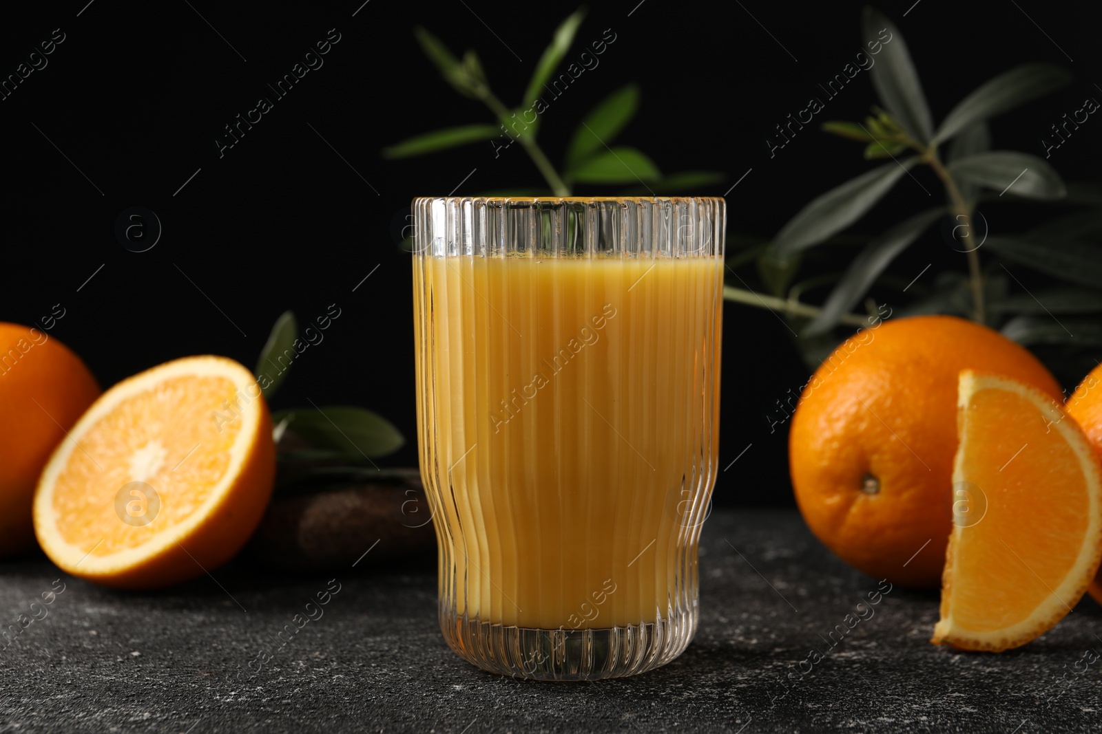 Photo of Tasty fresh oranges, juice and leaves on black table, closeup