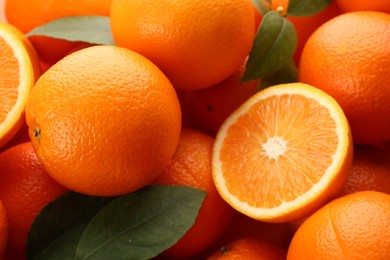 Photo of Cut and whole fresh ripe oranges with green leaves as background, closeup