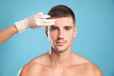 Photo of Doctor examining man's face for cosmetic surgery on light blue background