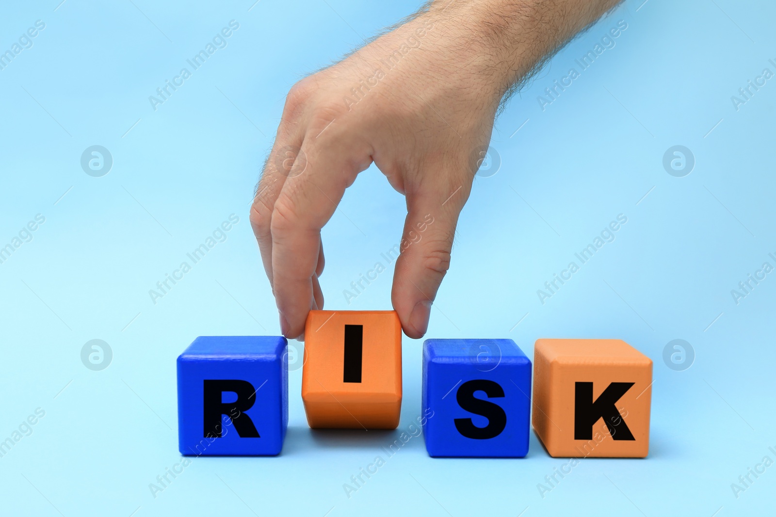 Photo of Man making word Risk of color wooden cubes on light blue background, closeup