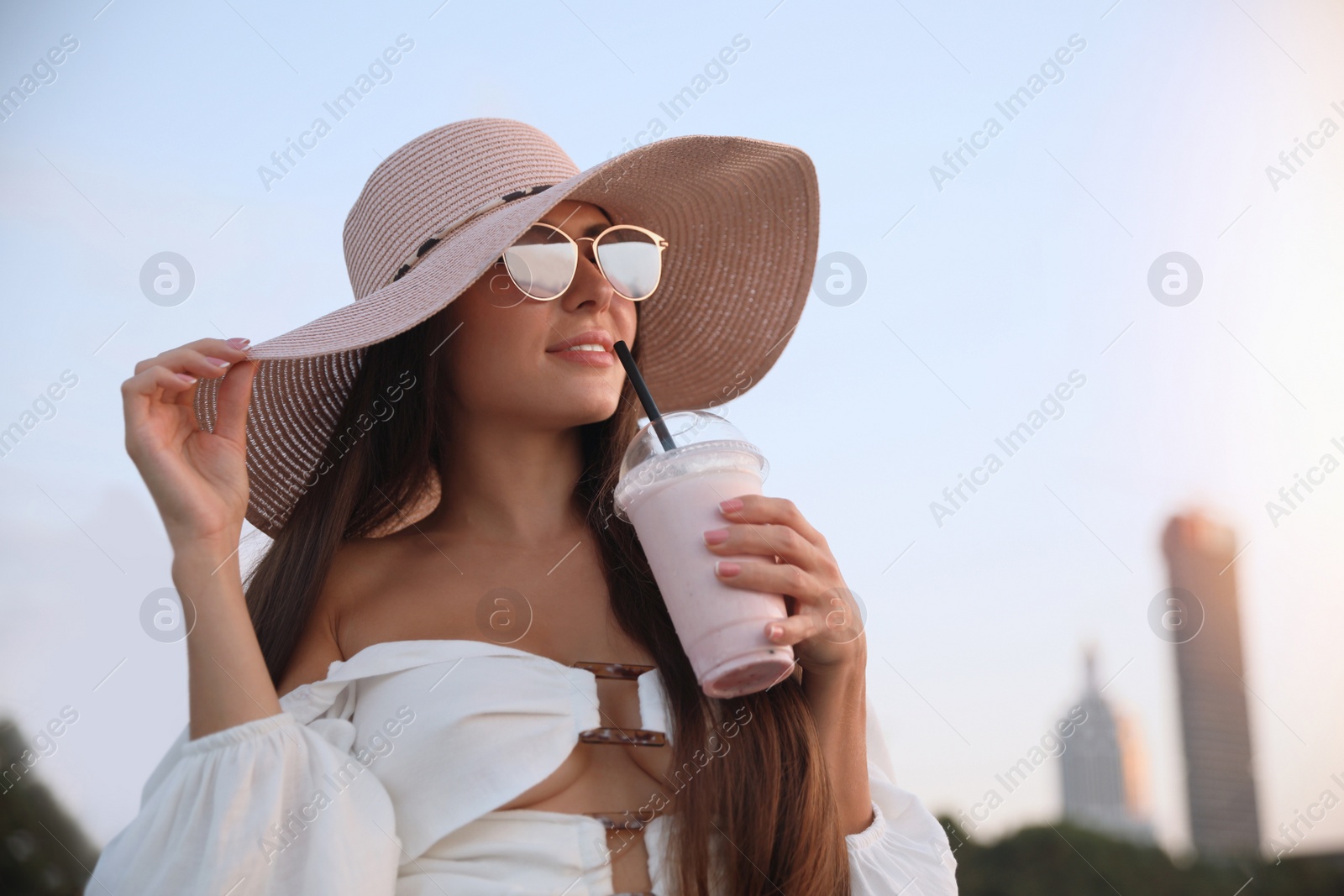 Photo of Beautiful young woman with tasty milk shake outdoors. Space for text