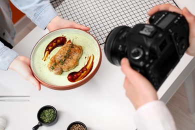 Photo of Food stylist holding plate with delicious meat medallion while photographer taking photo in studio, closeup
