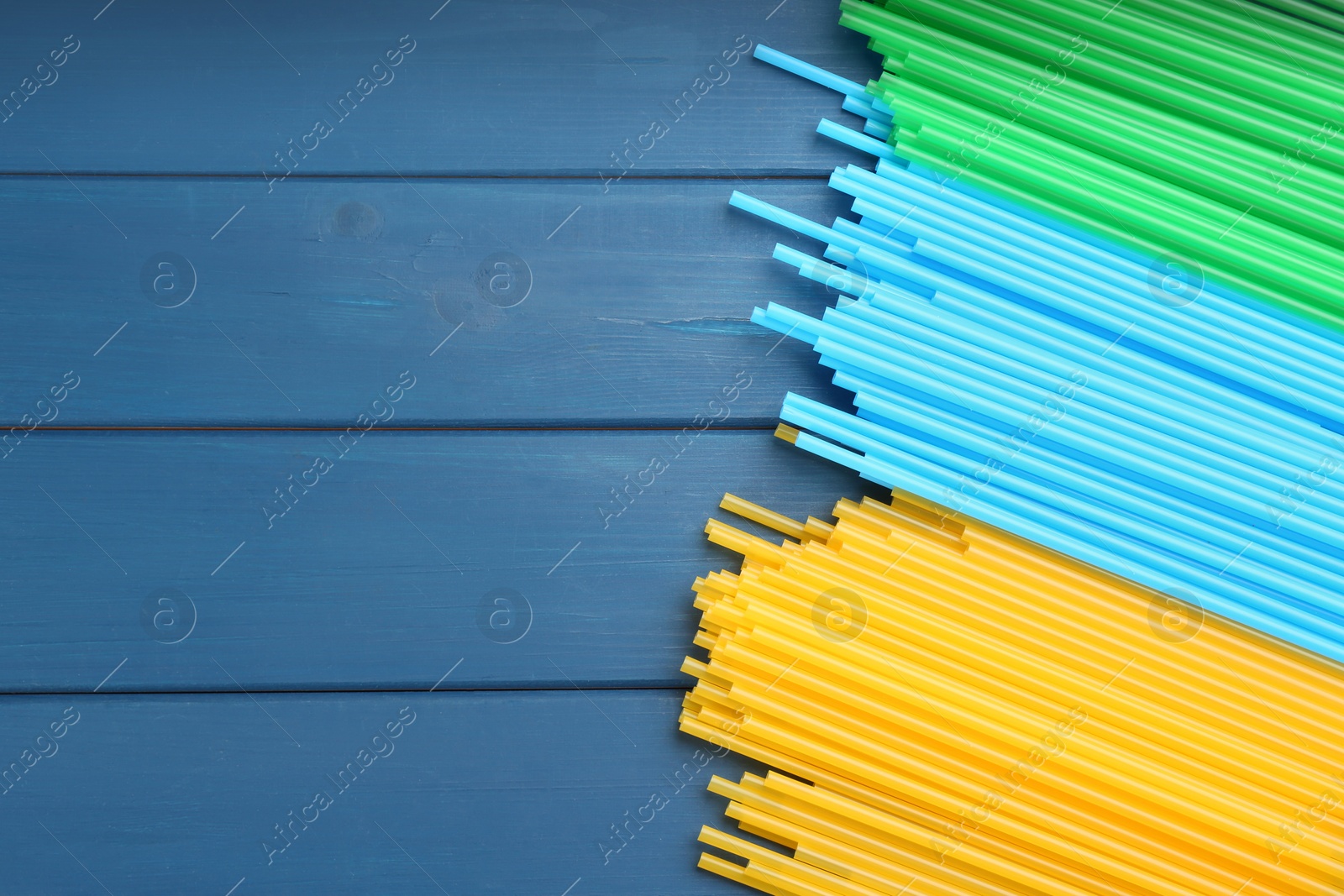 Photo of Colorful plastic drinking straws on blue wooden table, flat lay. Space for text
