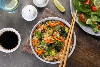 Tasty fried rice with vegetables served on grey table, flat lay