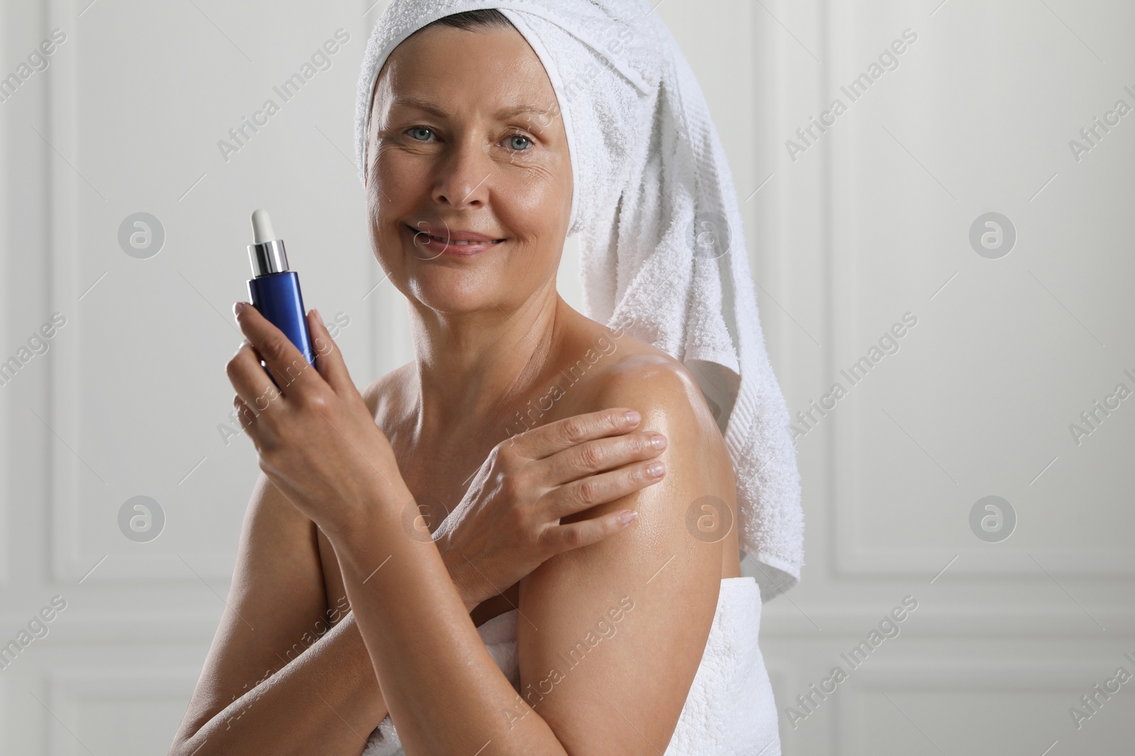 Photo of Happy woman applying body oil onto shoulder near white wall. Space for text