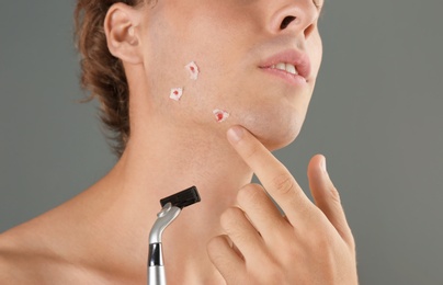 Young man with face hurt while shaving on gray background