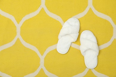 Photo of Soft fluffy white slippers on yellow carpet, top view. Space for text