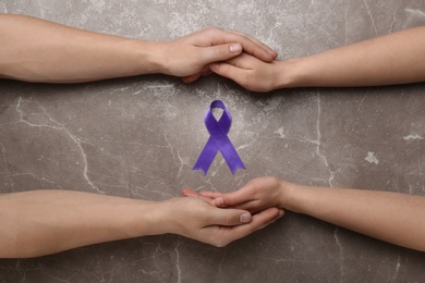 Man and woman holding hands and purple awareness ribbon on marble background, top view