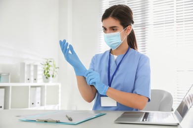 Doctor in protective mask putting on medical gloves at table in office