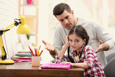 Father scolding his daughter while helping with homework at table indoors