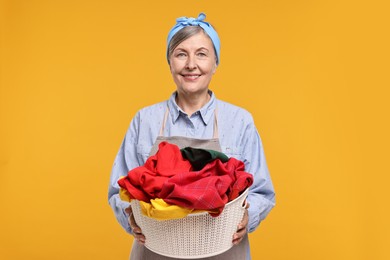 Happy housewife with basket full of laundry on orange background