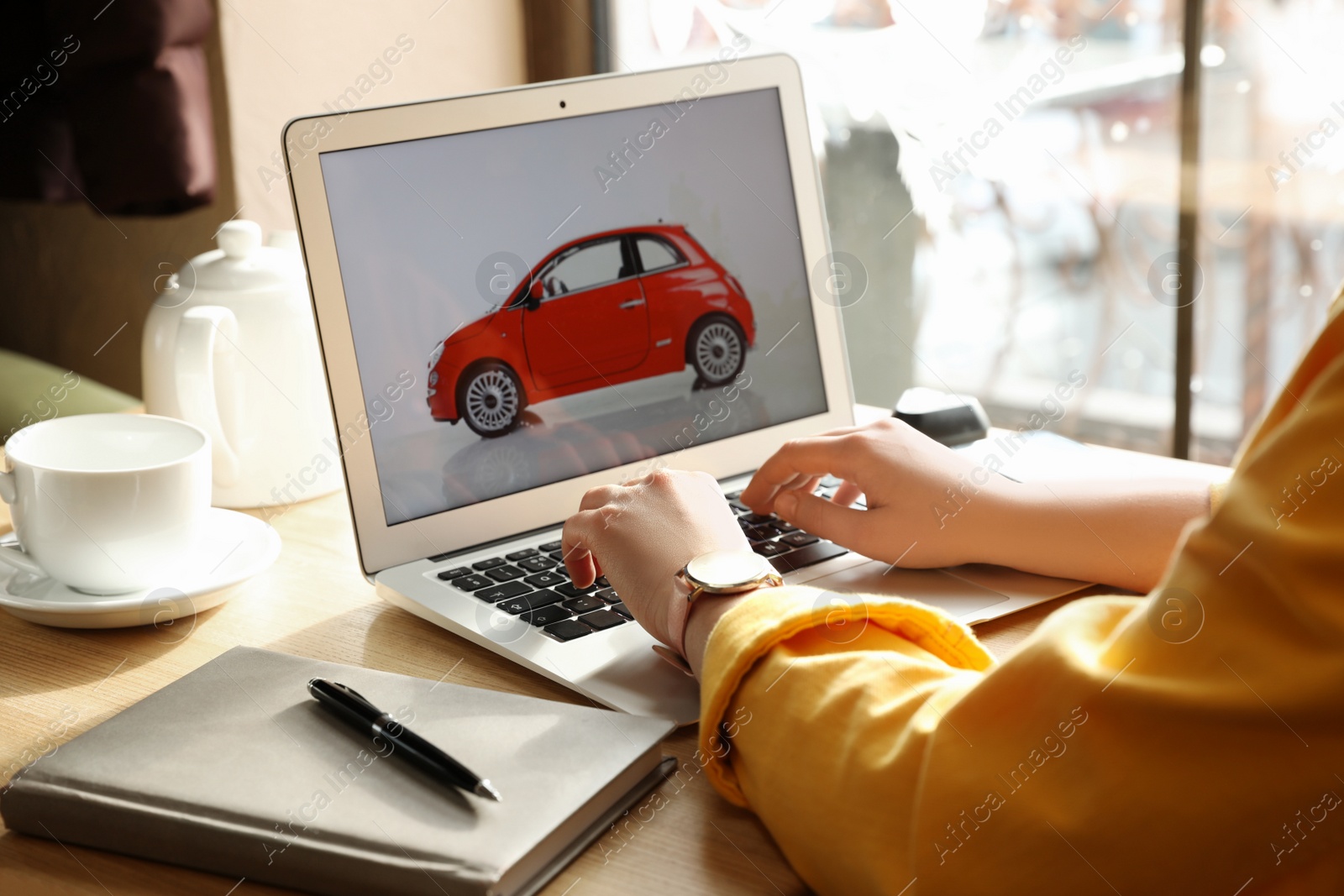 Photo of Woman using laptop to buy car at wooden table indoors, closeup