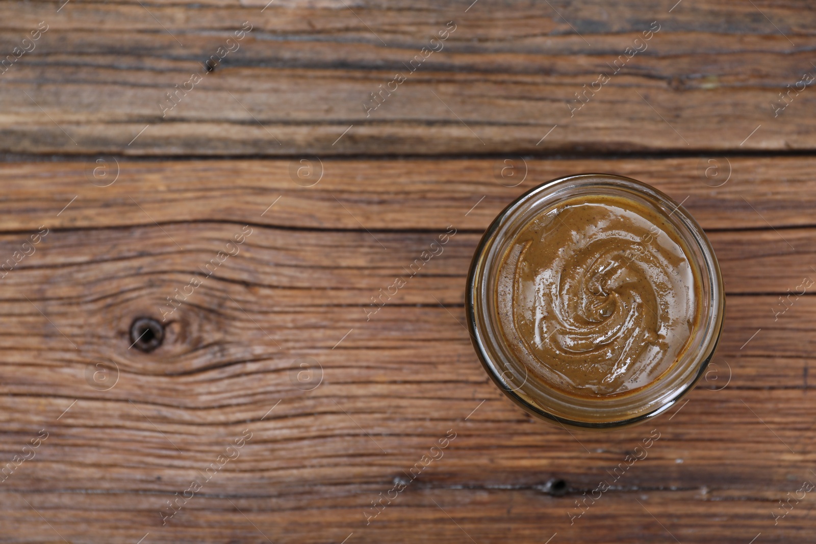 Photo of Tasty nut paste in jar on wooden table, top view. Space for text