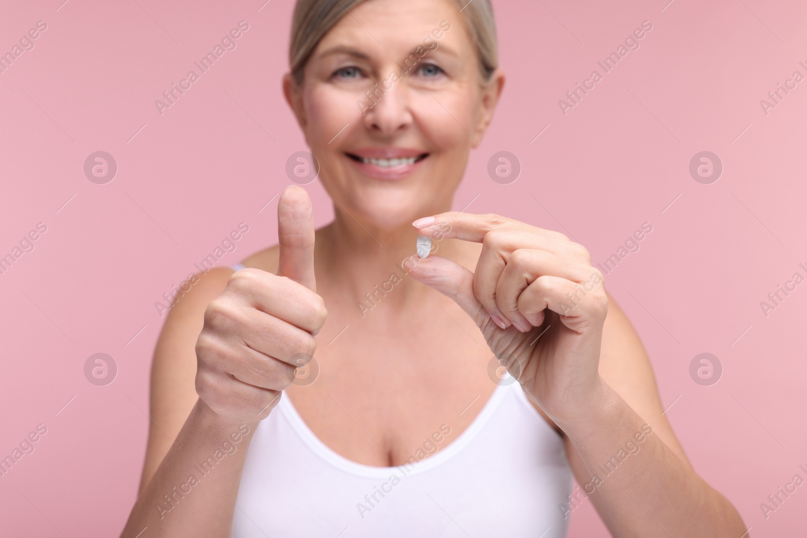 Photo of Beautiful woman with vitamin pill showing thumbs up on pink background, selective focus