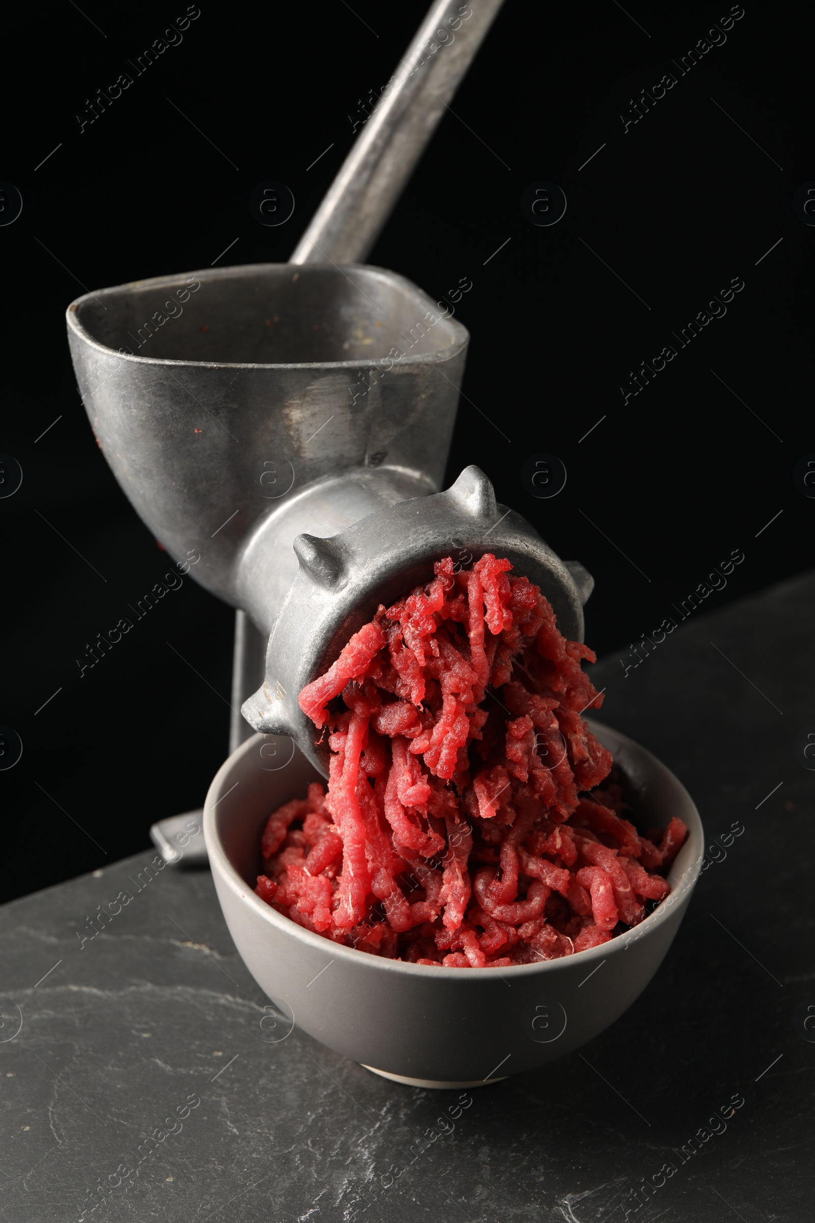 Photo of Metal meat grinder with beef mince on dark textured table against black background