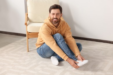 Photo of Man massaging leg on soft carpet at home