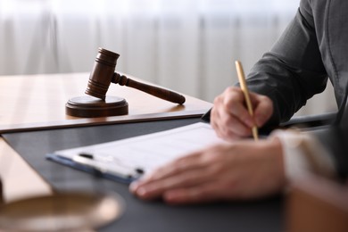 Notary writing notes at wooden table in office, closeup